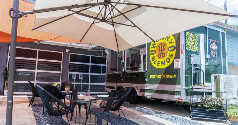 Outdoor seating area with black chairs and a large umbrella next to a food truck
