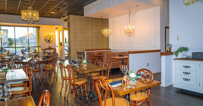 Interior of a restaurant with wooden tables, brown chairs, chandeliers, and large windows