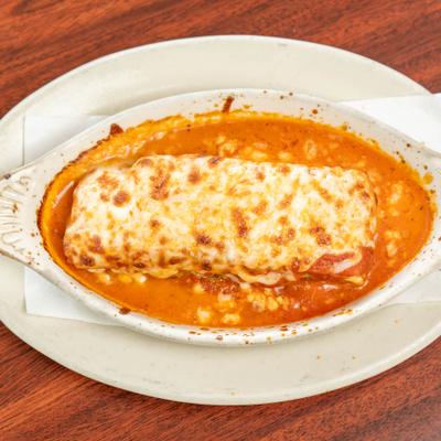 Baked lasagna in a red sauce served in an oval white dish.