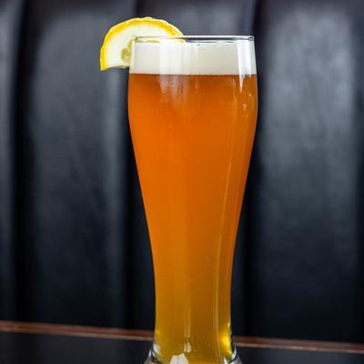 Glass of beer garnished with piece of lemon.