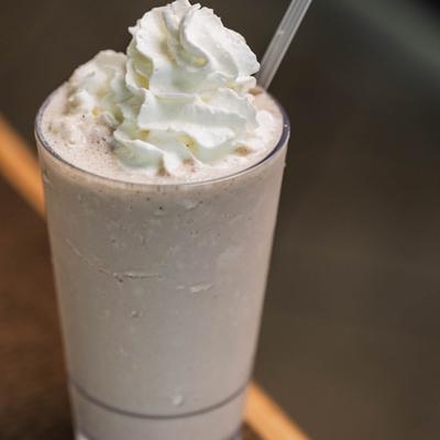 A milkshake topped with whipped cream and a clear straw, placed on a wooden table.