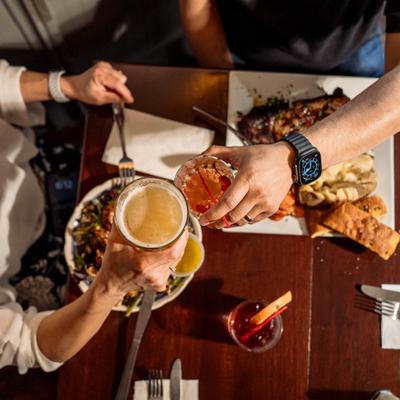 People toasting drinks over a table of food, overhead view.