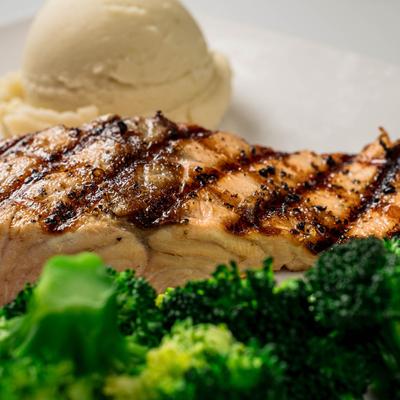 Grilled salmon with char marks, served with broccoli and a scoop of mashed potatoes.