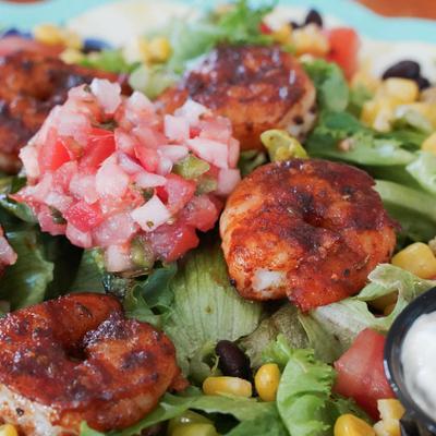 A close-up of a shrimp salad with mixed greens, corn, tomatoes, and beans.