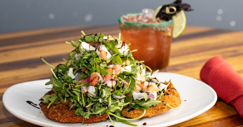 Panko Chicken Milanese topped with arugula salad and a cocktail