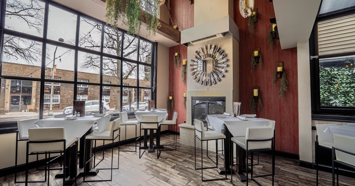 Modern interior - large windows, white tables and chairs and a decorative mirror above a fireplace