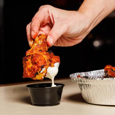 Buffalo chicken wings being dipped into a cup with sauce.