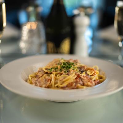 A plate with Spaghetti Carbonara served on a white table with sparkling wine.