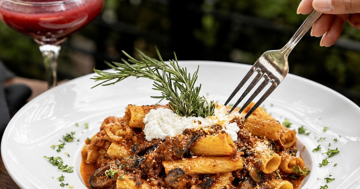 Rigatoni pasta with mushroom ragù, mascarpone, and rosemary, served beside a blackberry cocktail on the patio.