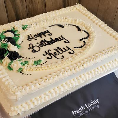 Rectangular birthday cake with white frosting, black and green floral decorations.