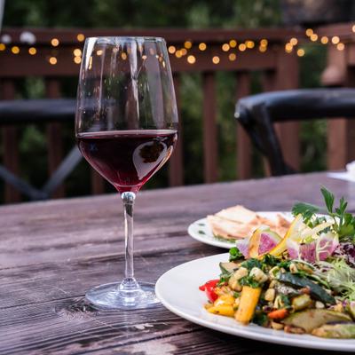 Glass of red wine served beside two plates of food.