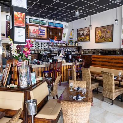 Interior with wicker chairs, set tables, wall art, and a stocked bar.