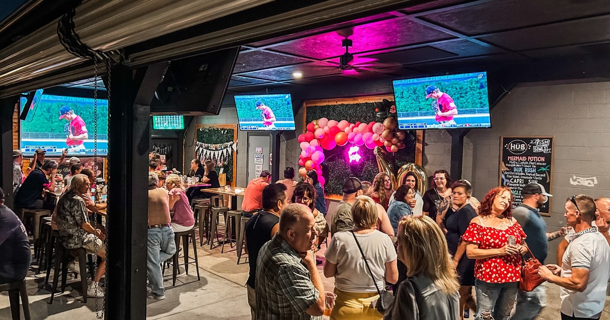 A busy sports bar with guests, TVs, and balloon decorations