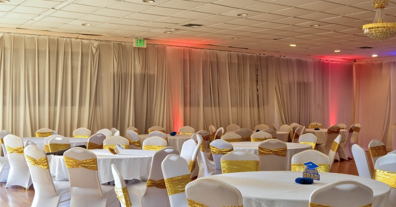 Banquet hall with round tables, white tablecloths, chairs with gold sashes, and a ceiling chandelier