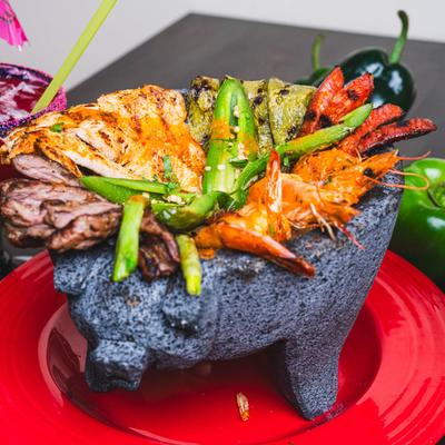 Molcajete, with various meats, cheese, green sauce, and cheese.