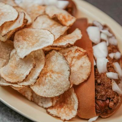 Chili hot dog served with potato chips.