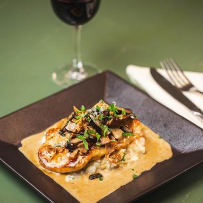 A plate of Chicken Marsala and glass of red wine behind.