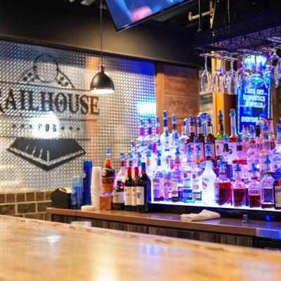 Fully stocked bar with various illuminated bottles and an overhead glass rack.