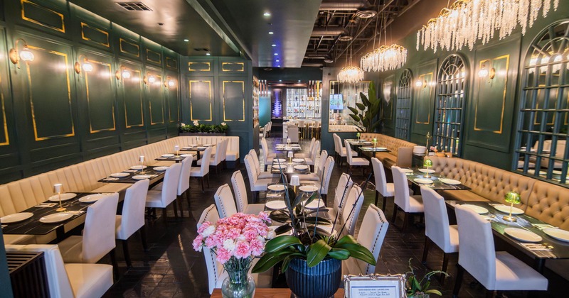 An elegant restaurant interior with white table settings, cushioned seating, and crystal chandeliers