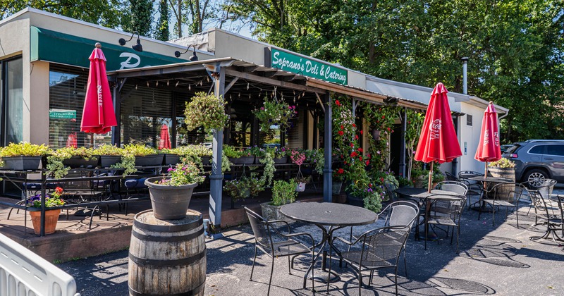 Outdoor seating area of a deli with tables, chairs, red umbrellas