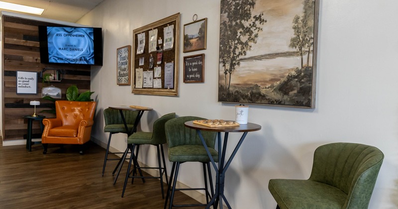 Cozy interior - orange armchair, TV screen, corkboard, paintings, and tables with green chairs