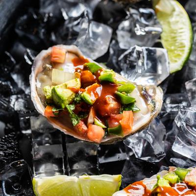 Fresh oyster on ice topped with avocado, tomato, sauce, and onion.