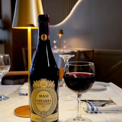 A bottle of red wine beside a filled glass on a dinner table.