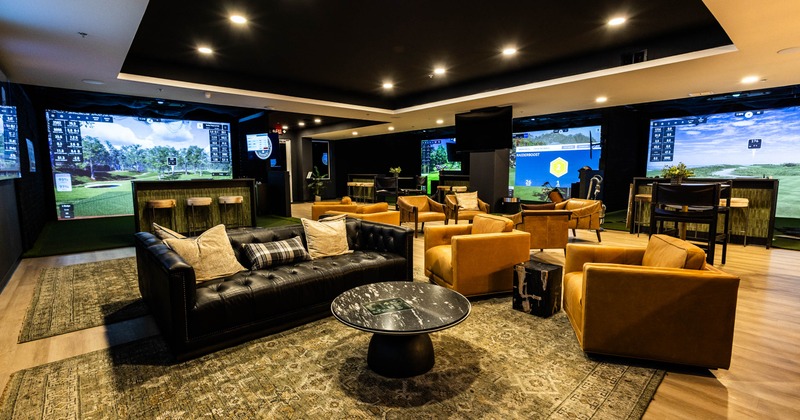 A modern lounge with golf simulators, leather seating and large screens