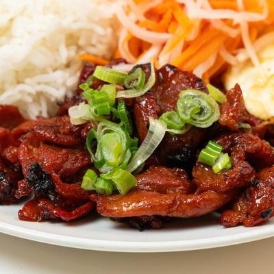 Grilled pork BBQ topped with green onion, served with broken rice and pickled vegetables.