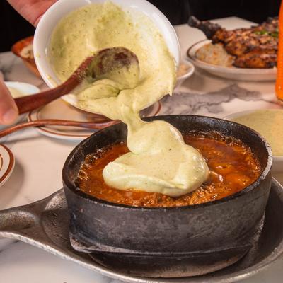 Creamy green sauce being poured over a bowl of lamb stew.