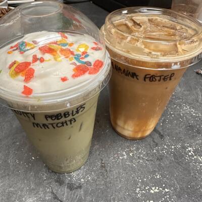 An iced Fruity Pebbles Matcha Latte topped with Cold Foam and Fruity Pebbles alongside an iced Bananas Foster Latte.