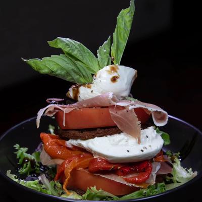 A salad stack with layers of tomato, eggplant, mozzarella, and prosciutto.
