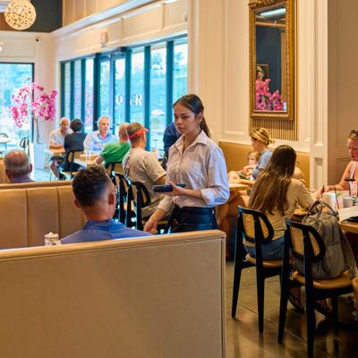 Restaurant interior with patrons seated at tables and a staff member assisting guests.
