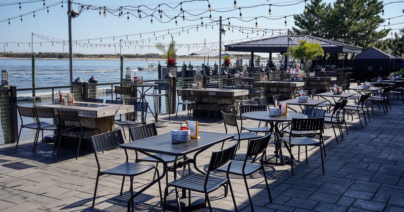 Outdoor dining area by the waterfront, tables and string lights above