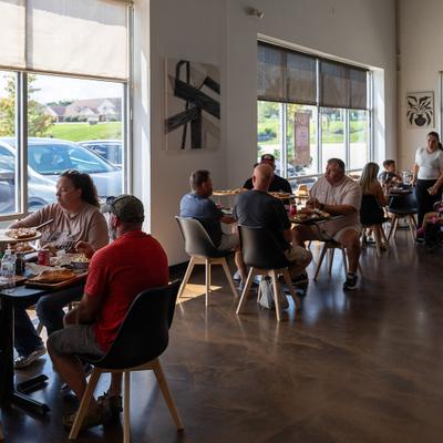 The interior of dining area with customers sitting at tables near large windows.