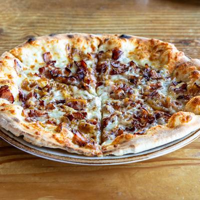 A pizza on a wooden table, topped with cheese, caramelized onions, and crispy bacon.