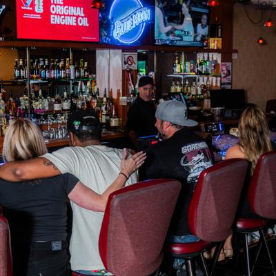 Group of people socializing at the bar counter with multiple TV screens.