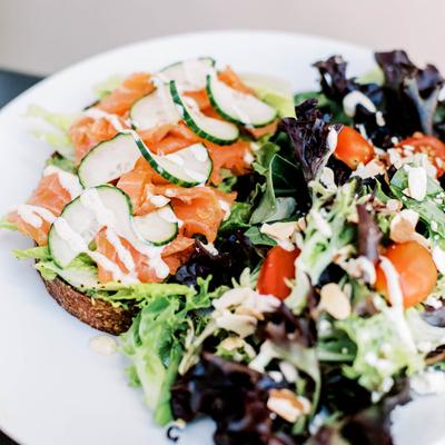 Avocado toast topped with smoked salmon, cucumbers, and aioli, served with a mixed spring salad.