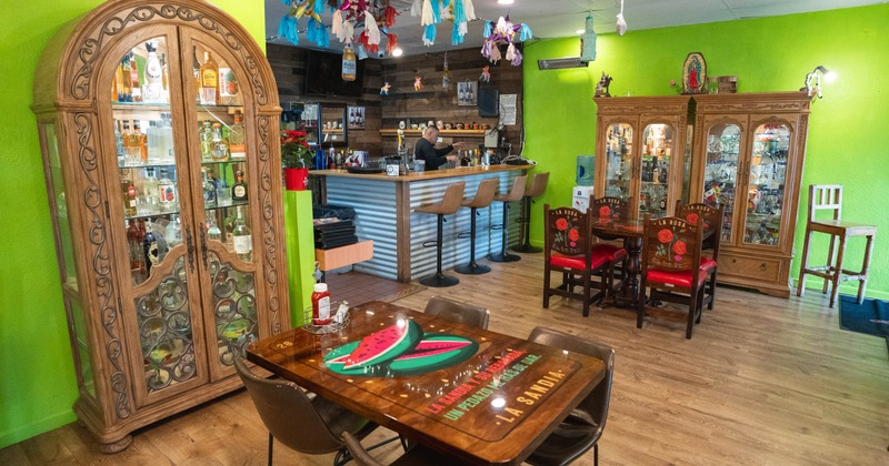 Interior of a colorful restaurant with tables, chairs, a bar, and display cabinets