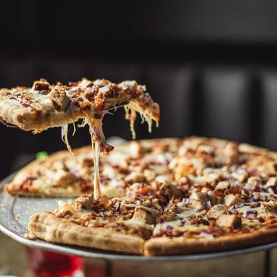 A slice of chicken pizza with melty cheese being lifted from the pie.