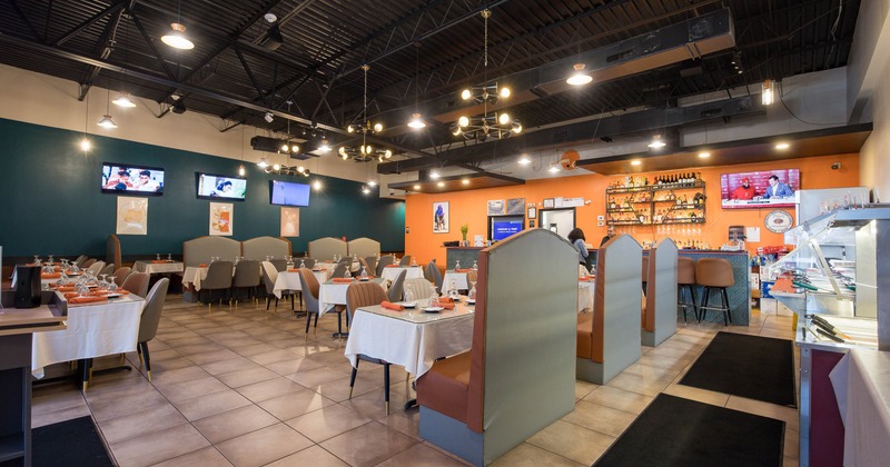 A modern interior - white tablecloths, plush seating, TVs on the walls and decorative shelves