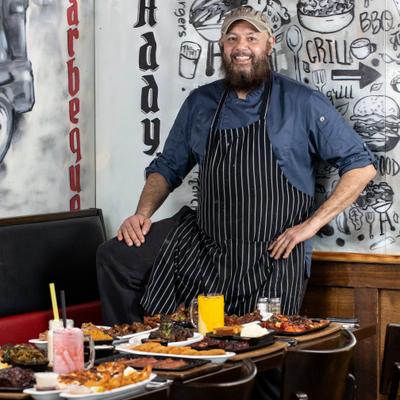Chef standing in front of the table with food and drinks.
