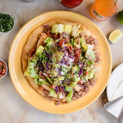 Chicken tostada with beans, lettuce, cabbage, and tomatoes.