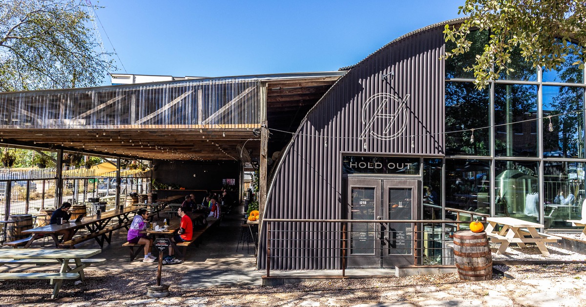 Rustic interior with exposed ductwork, wooden floors, tables, a central bar and a large window.