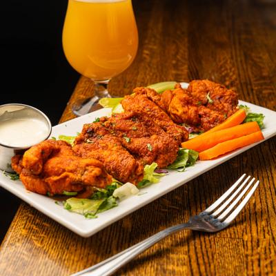 Chicken wings on a bed of lettuce with carrots, ranch dip, and a glass of beer.
