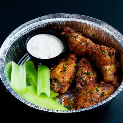 Seasoned chicken wings with celery sticks and creamy dipping sauce in an aluminum foil container.