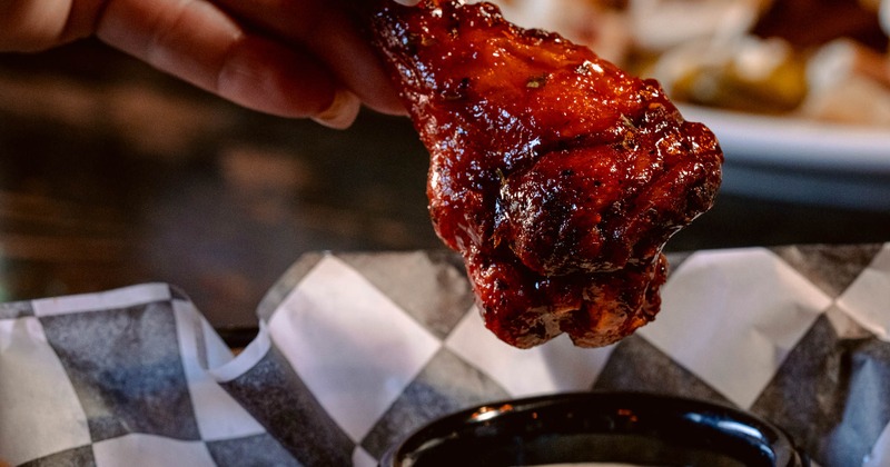 Glazed chicken wing held above the cup of sauce, close-up