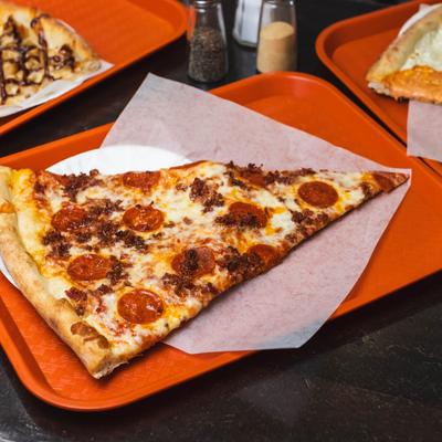 A slice of pepperoni and bacon pizza on a tray.