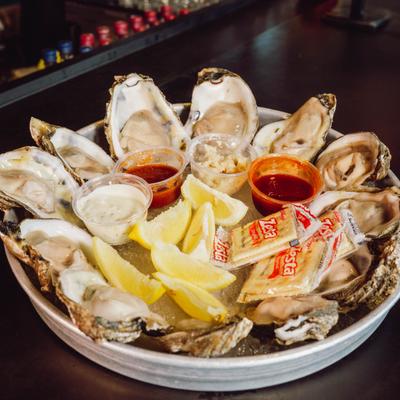 Raw oysters on ice with crackers, sauces, and lemon wedges.