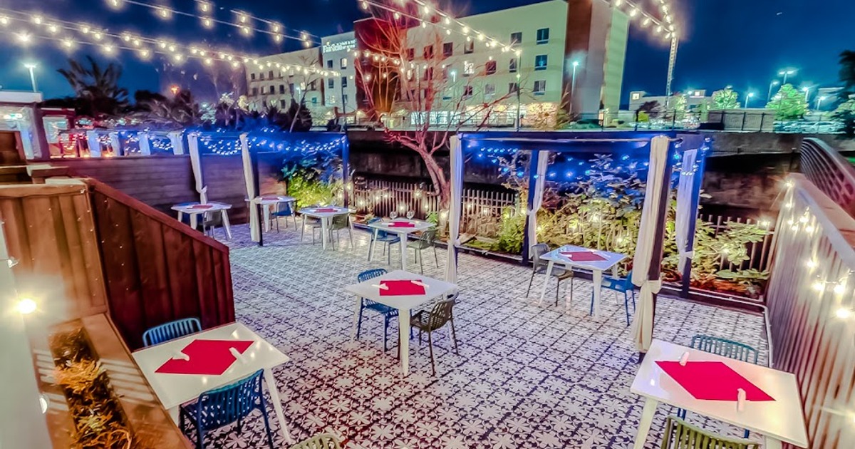 A nighttime patio scene with, string lights,  tables and chairs